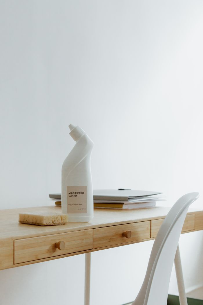 A tidy, well-arranged home office desk with a cleaning bottle and sponge, highlighting practicality and simplicity.